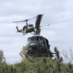 Helicóptero UH-1H matrícula AE-471 de la Aviación de Ejército Argentino en vuelo rasante con tropas a bordo, acompañado por un segundo Huey en formación.
