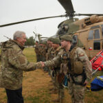Autoridad de gobierno saluda a efectivos de rescate del Ejército de Chile frente a un helicóptero de transporte durante el despliegue militar por el sistema frontal.