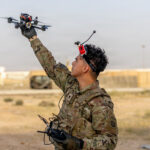 Militar lanza con la mano un dron FPV mientras sostiene el control de radiofrecuencia con gafas de vuelo sobre la frente.