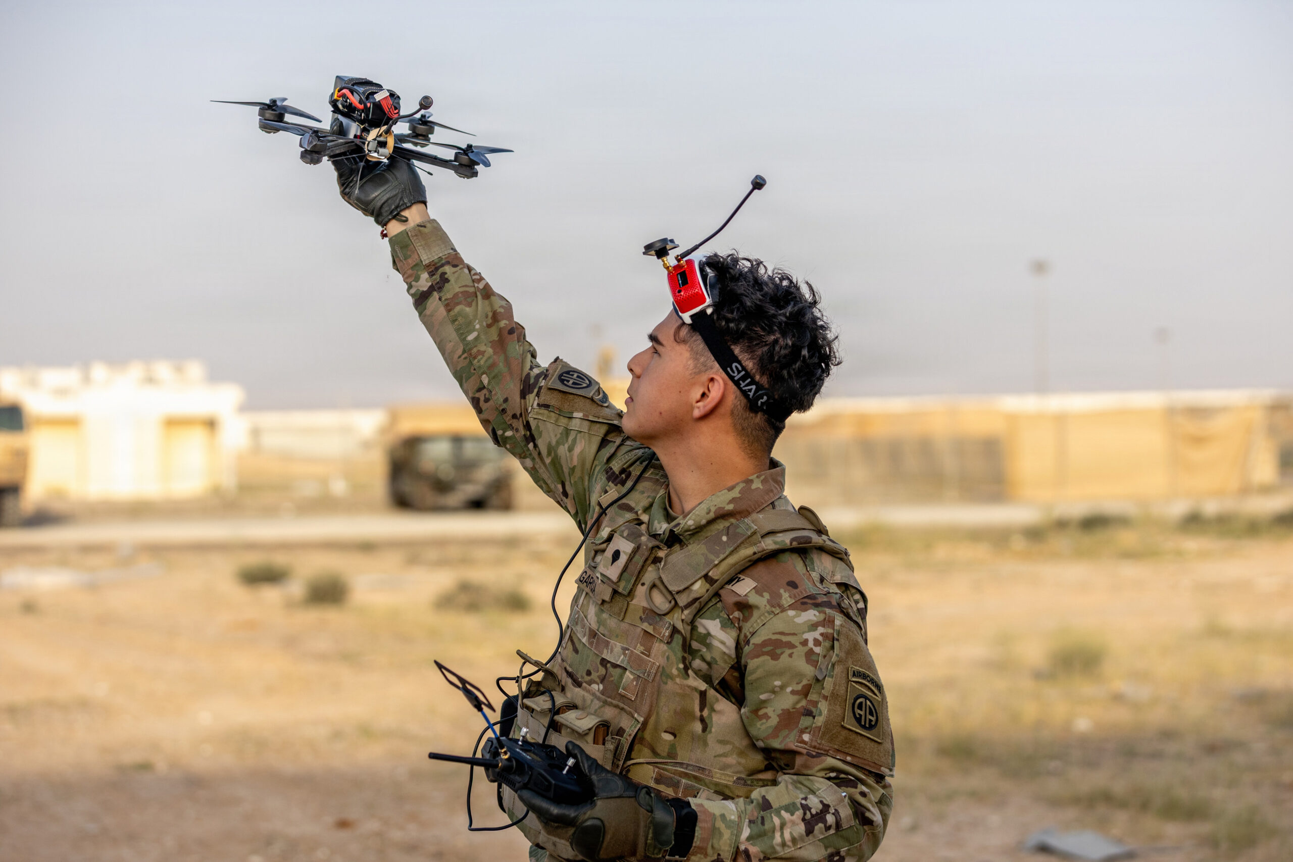 Militar lanza con la mano un dron FPV mientras sostiene el control de radiofrecuencia con gafas de vuelo sobre la frente.