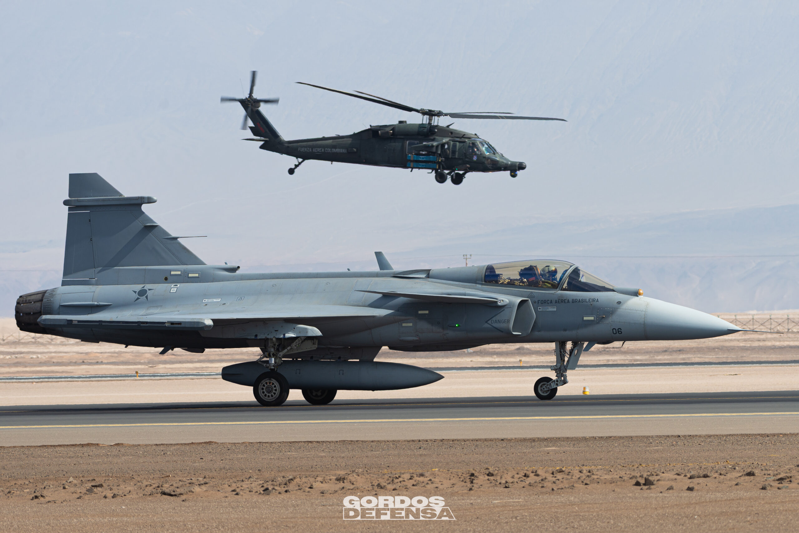 Caza Gripen de la Fuerza Aérea Brasileña en pista con un Black Hawk colombiano al fondo