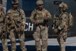 Operadores de fuerzas especiales con el rostro cubierto y equipo táctico junto a un helicóptero