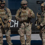 Operadores de fuerzas especiales con el rostro cubierto y equipo táctico junto a un helicóptero