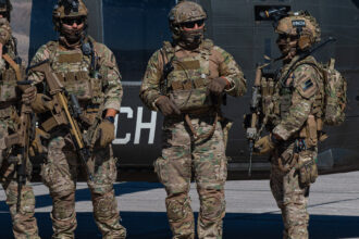 Operadores de fuerzas especiales con el rostro cubierto y equipo táctico junto a un helicóptero