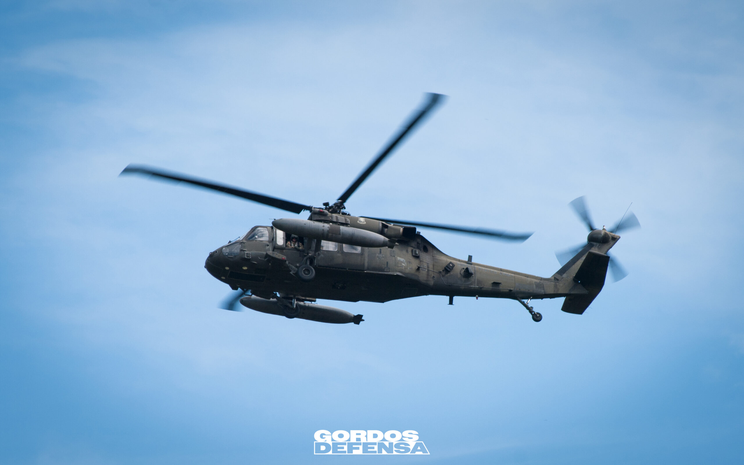 Helicóptero UH-60 Black Hawk utilitario en vuelo de perfil contra cielo azul, con tanques de combustible externos