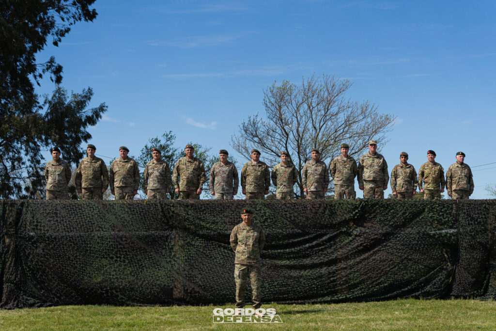 Grupo de oficiales del Ejército formados sobre un palco cubierto con red de camuflaje, con un oficial parado al frente
Título: Acto de incorporación del segundo escuadrón de TAM 2C-A2