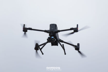 Dron cuadricóptero negro con una cámara multisensor montada debajo, visto desde abajo en vuelo contra el cielo nublado