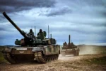 Dos tanques K2 Black Panther con tripulantes en las escotillas avanzando por un camino de tierra bajo un cielo nublado