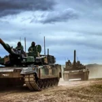 Dos tanques K2 Black Panther con tripulantes en las escotillas avanzando por un camino de tierra bajo un cielo nublado