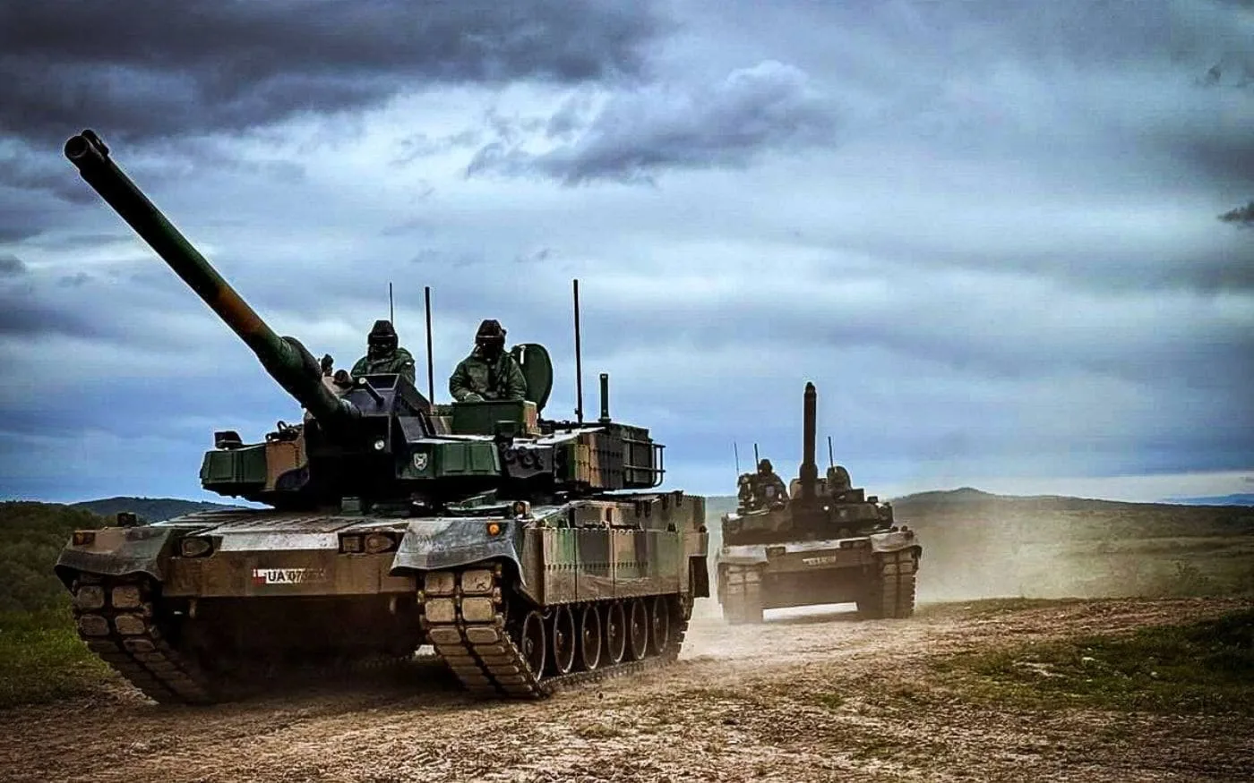 Dos tanques K2 Black Panther con tripulantes en las escotillas avanzando por un camino de tierra bajo un cielo nublado